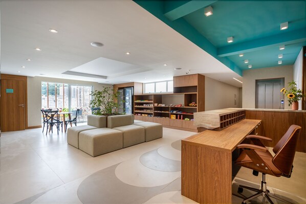 Un espace d’accueil moderne avec un bureau en bois, des fauteuils en cuir, un coin salon avec un canapé et une grande fenêtre laissant entrer la lumière naturelle.