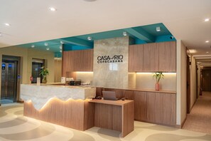 Un comptoir d’accueil moderne, doté d’un plateau en marbre, de panneaux en bois et d’une enseigne indiquant « CASA RIO COPACABANA ».