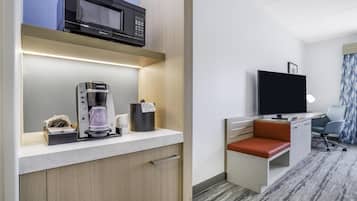 Ein Hotelzimmer mit Küchenzeile, einem Flachbildfernseher, einer Sitzecke mit gepolstertem Sitz und einem Teppichboden.
