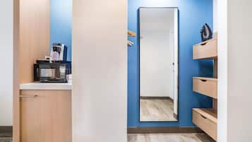 A kitchenette with a microwave, coffee maker, and hanging clothes rack.