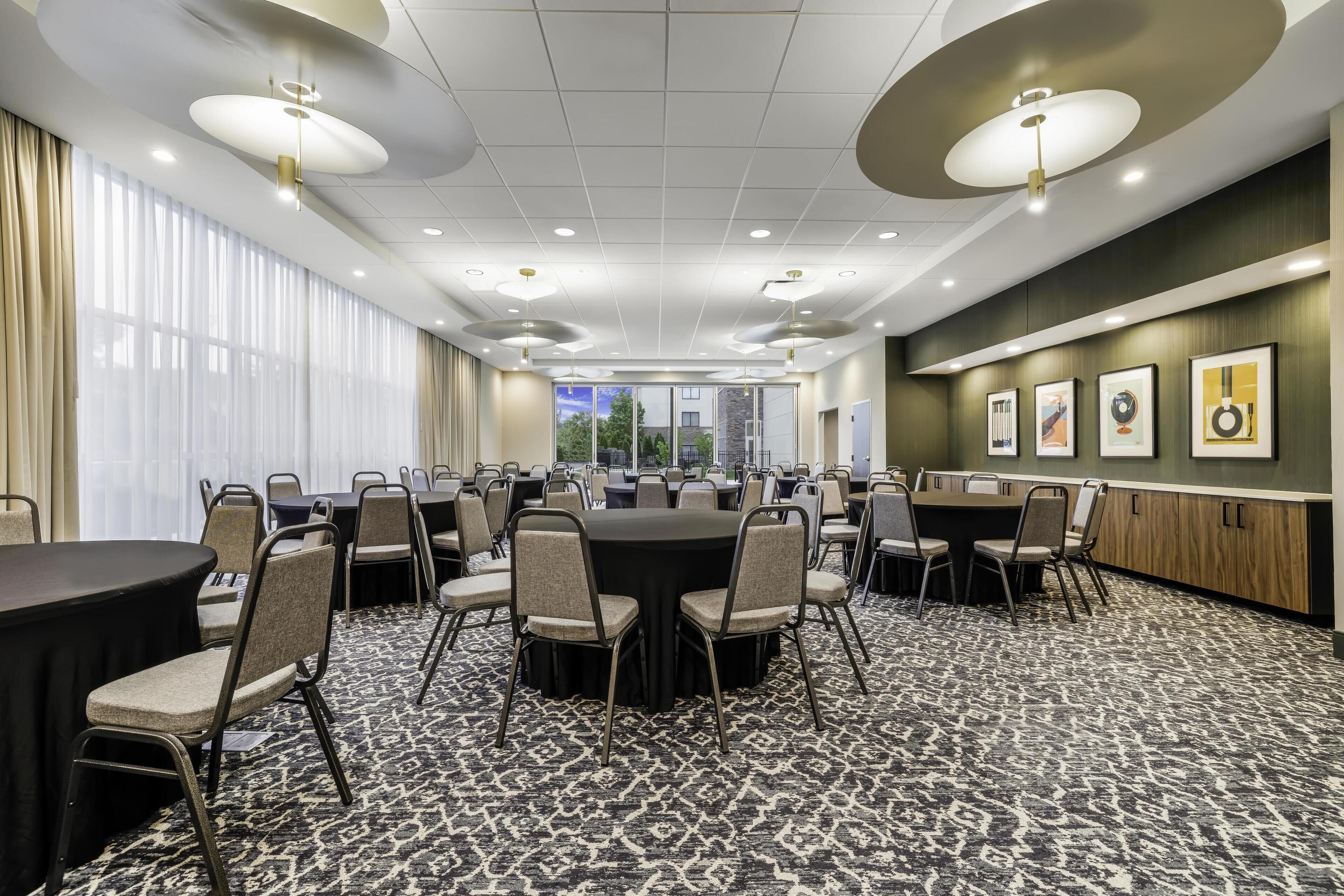 A conference room with round tables and chairs, large windows, and framed artwork on the walls.