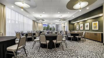 A conference room with round tables and chairs, large windows, and framed artwork on the walls.