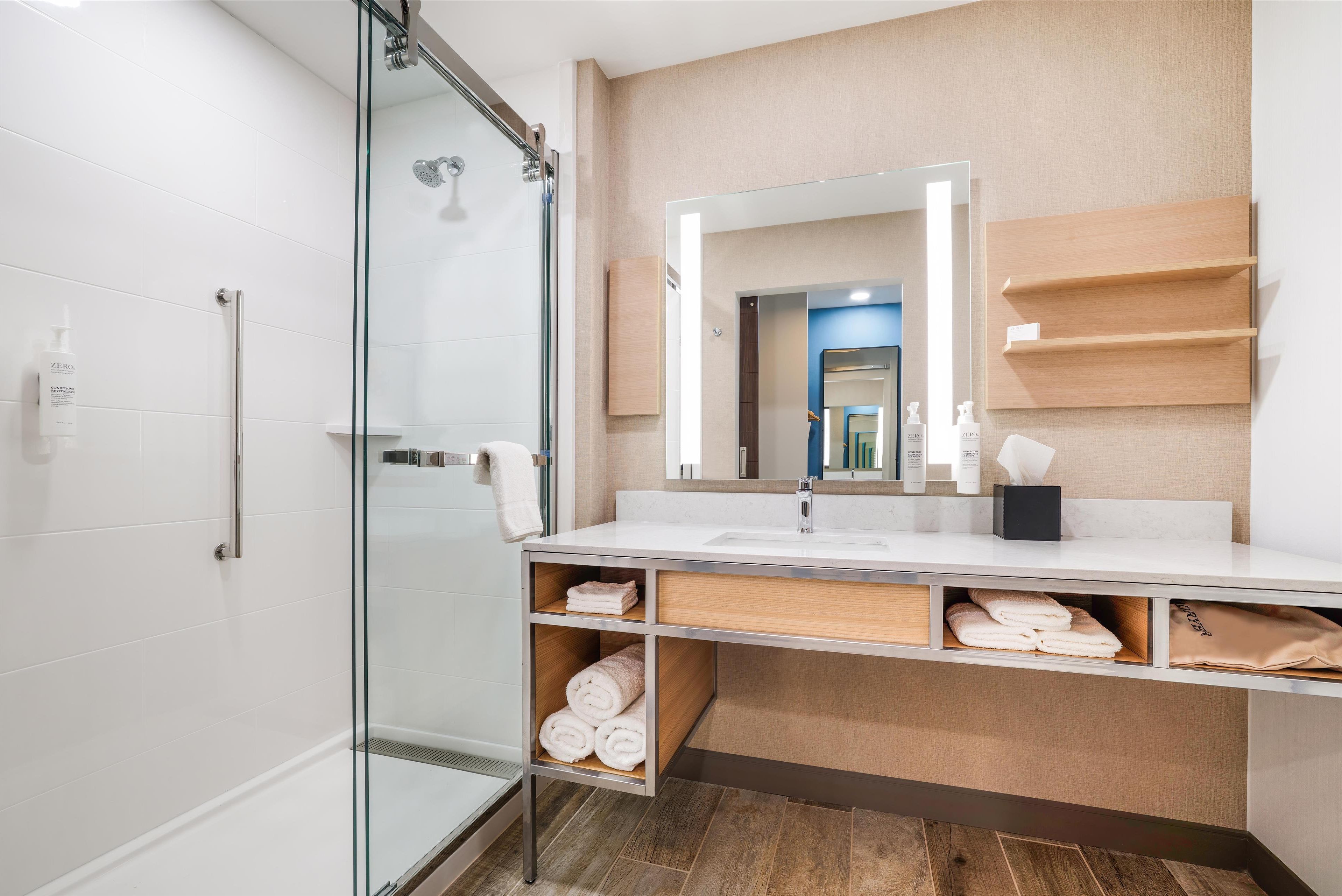 A modern bathroom with a glass shower enclosure, a large mirror, and built-in towel storage.