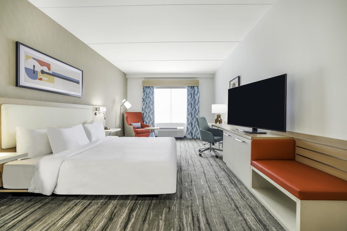 Quarto de hotel com uma cama grande, uma escrivaninha, televisão e área de estar.