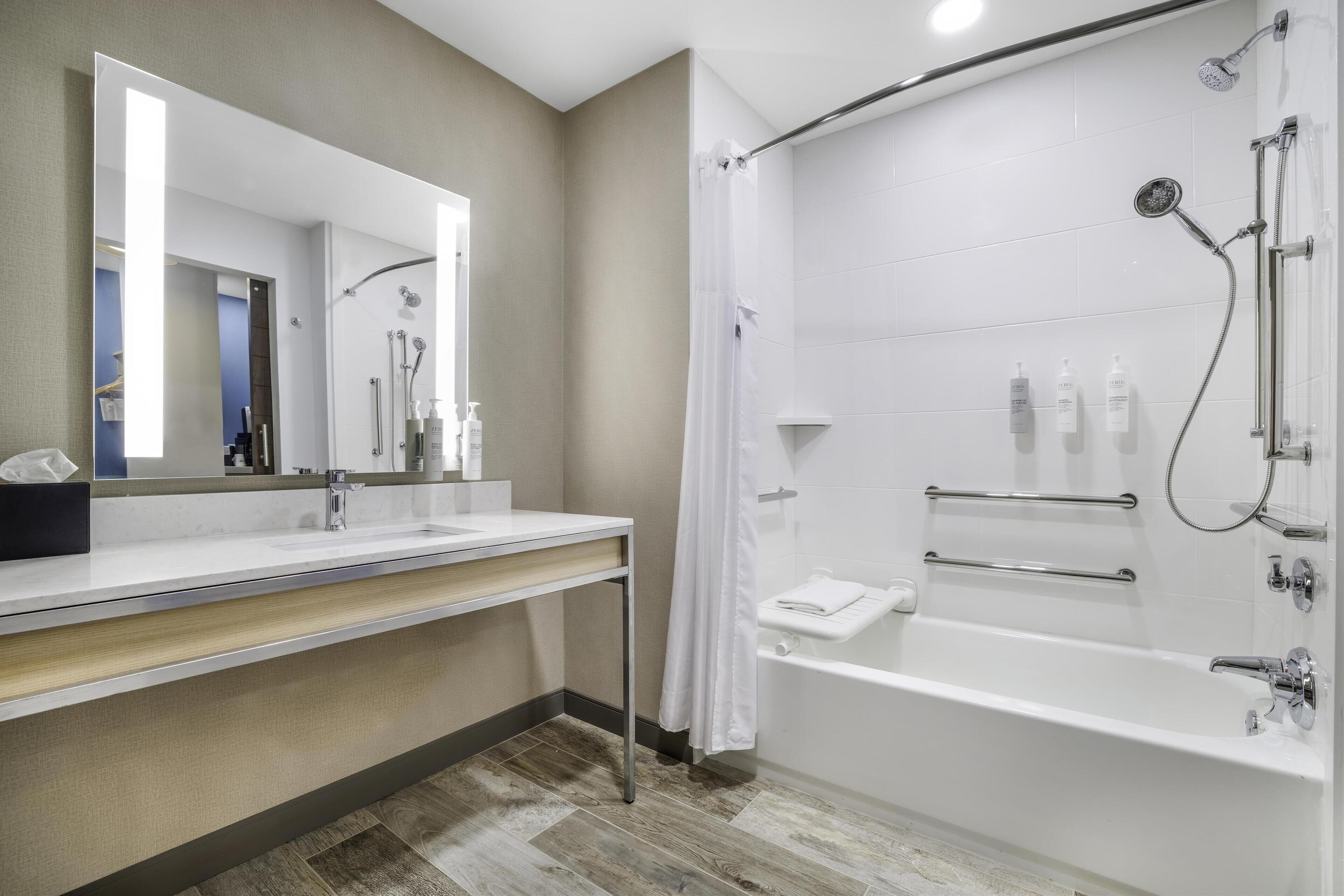 Un baño moderno con un espejo grande, un lavamanos, una ducha con cortina y una bañera.