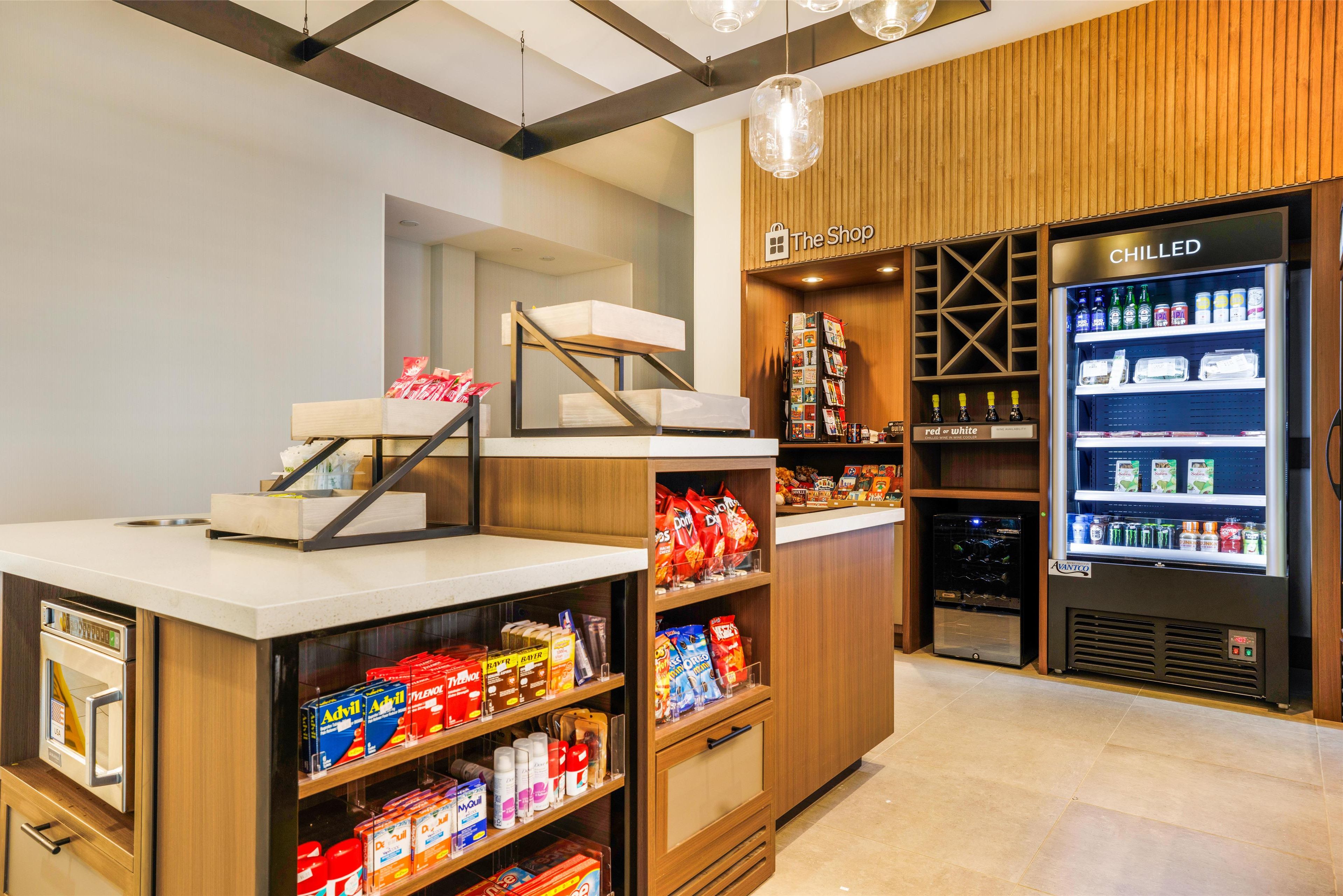 Una tienda con mostrador de madera, estantes llenos de aperitivos y bebidas, y una sección refrigerada con la etiqueta 'CHILLED'.