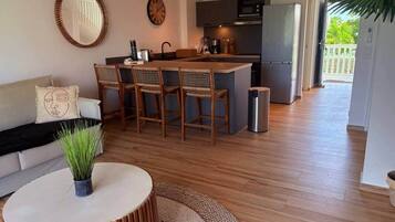 A modern kitchen with a central island, a dining area with wicker chairs, a round coffee table, and a sofa with a decorative pillow.