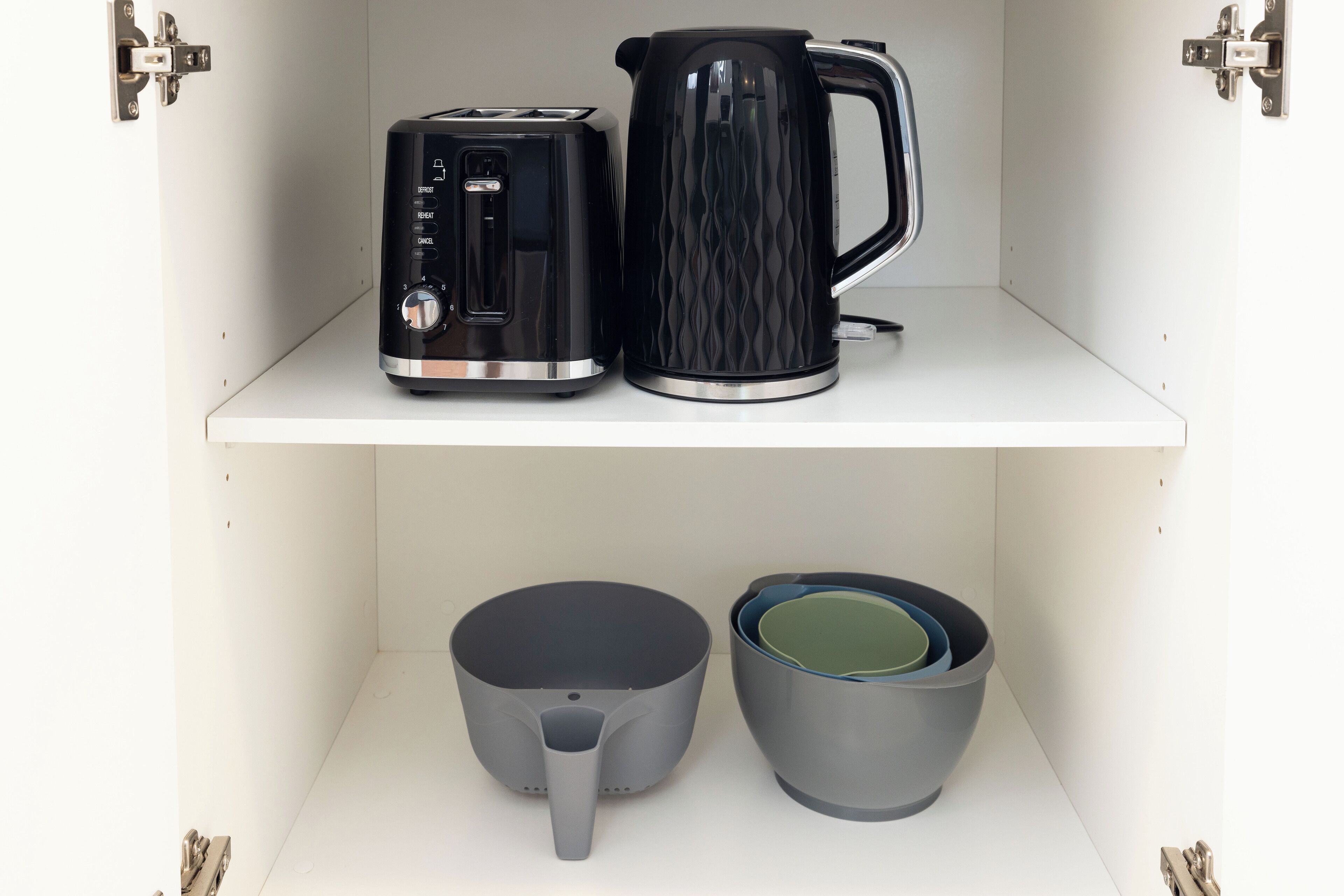A kitchen shelf with a toaster, a kettle, a large pot, and two mugs.
