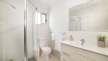 Et moderne badeværelse med brusekabine i glas, toilet i hvid farve, vask med spejl og en lille stueplante.