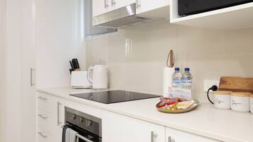 A modern kitchen with white cabinets, a black induction cooktop, a stainless steel range hood, a built-in oven, and a microwave.
