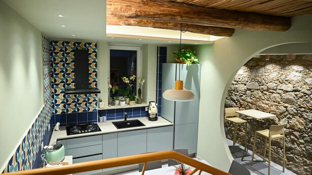 A modern kitchen with a geometric tile backsplash, a stone wall, and a rustic wooden ceiling.