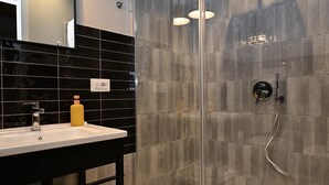 A modern bathroom with a black tiled wall, a glass shower enclosure, a white sink with a yellow soap dispenser, and a handheld showerhead.