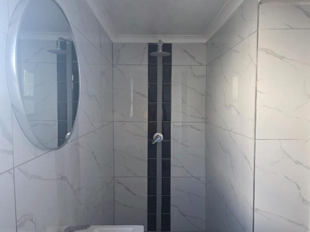 A bathroom with a shower, a mirror, and marble-patterned walls.