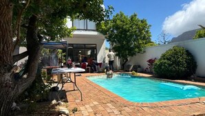A backyard with a swimming pool, a covered patio table, and a large tree. - Heaven  (Cape Town)