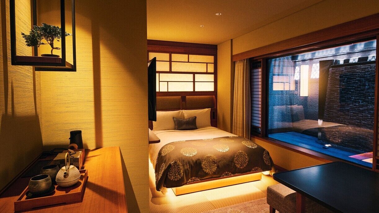 A hotel room with a bed, bedside table, and a window with a view.