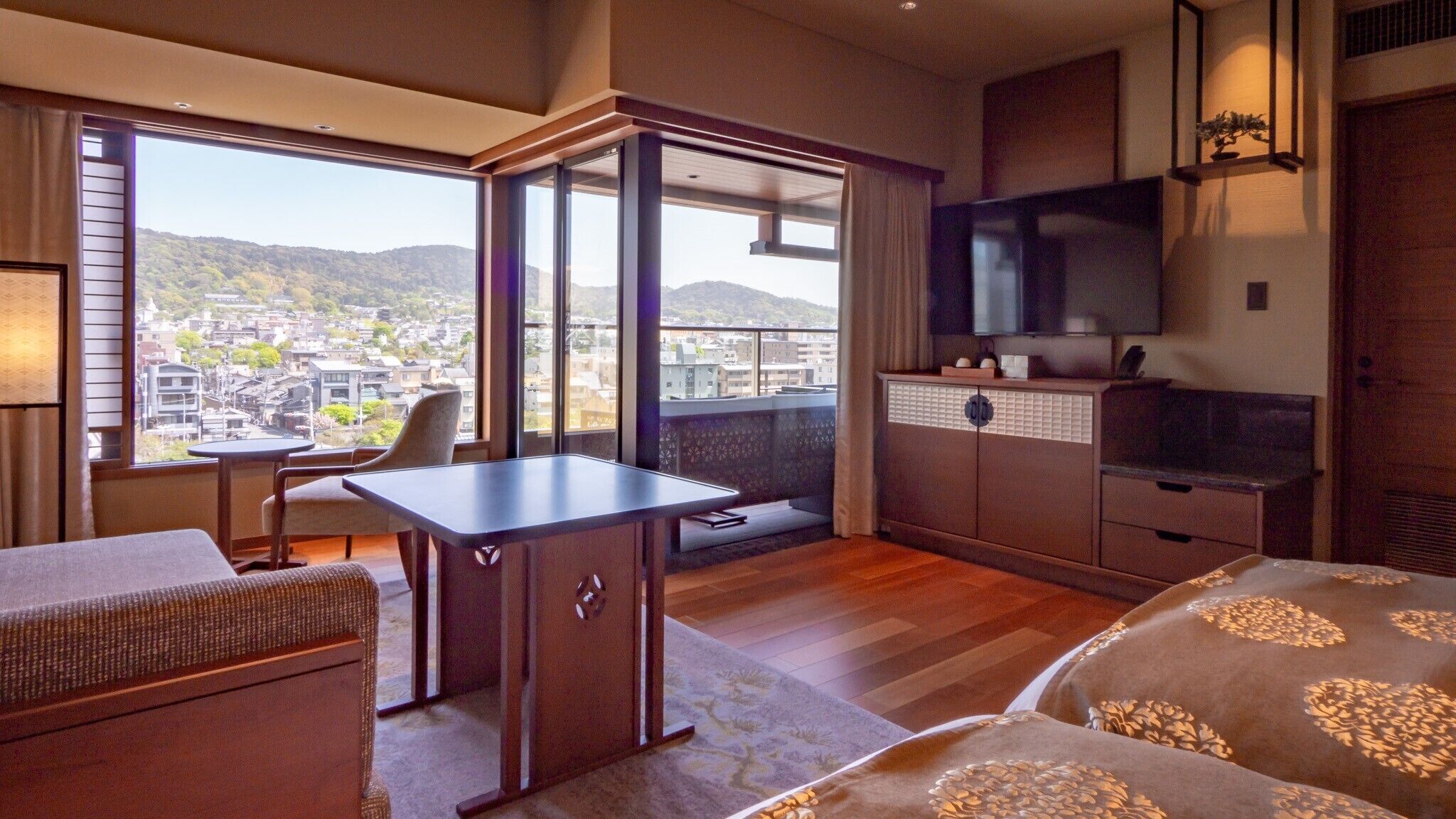 A hotel room with a balcony, a desk, a sofa, a TV, and a cabinet.