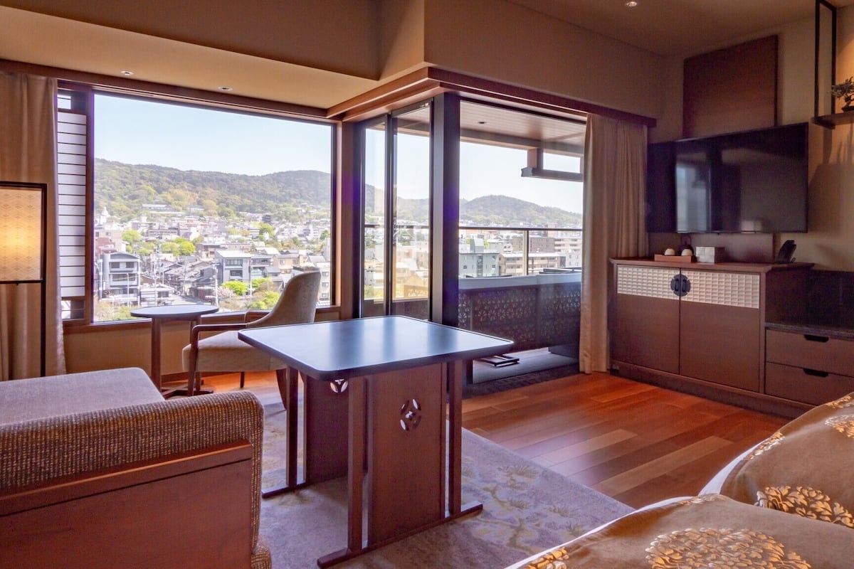 Ein Hotelzimmer mit Balkon, Schreibtisch, Sofa, Fernseher und Schrank.