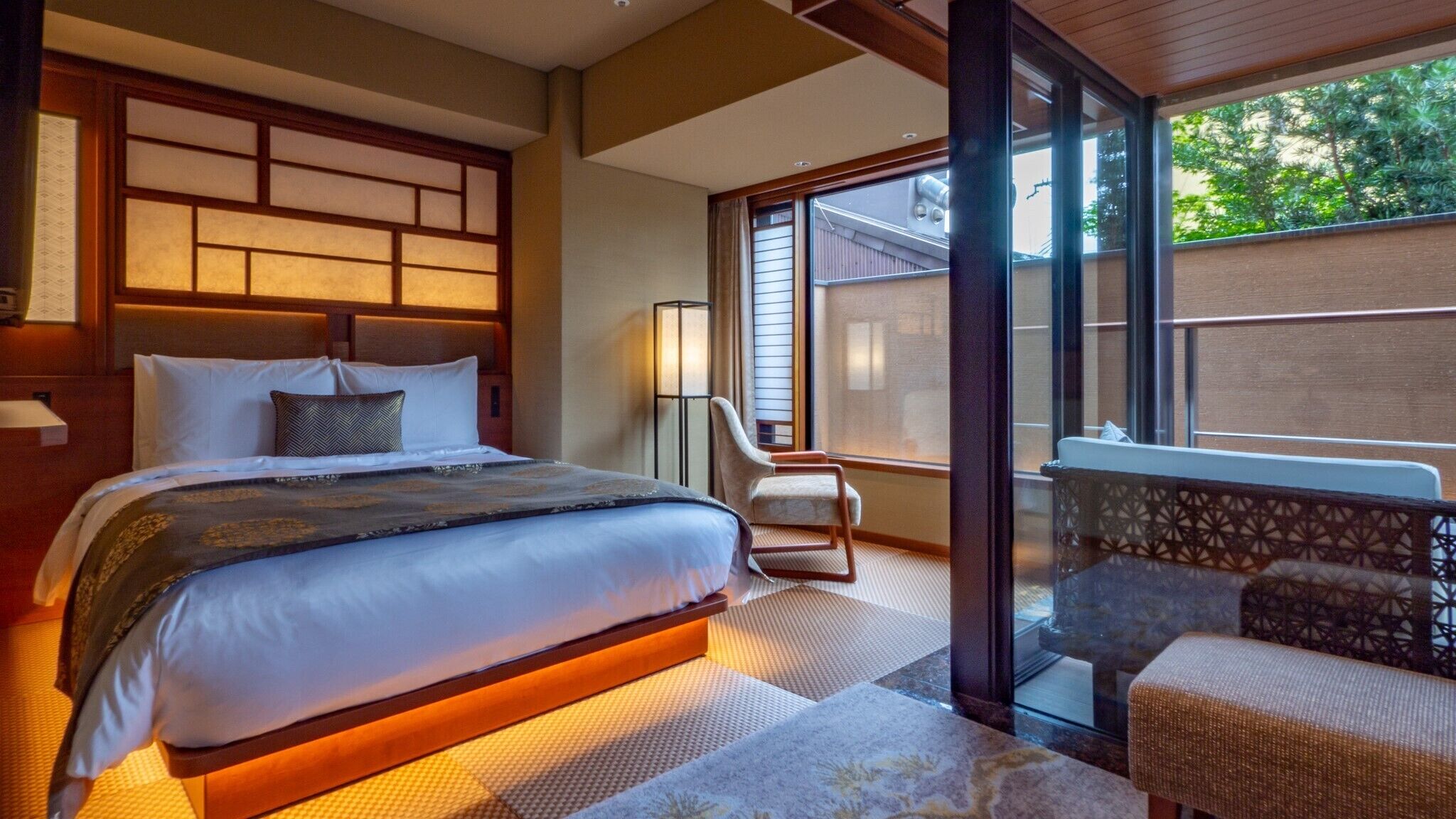 A hotel room with a large bed, a chair, a desk, and a view of the outdoors.
