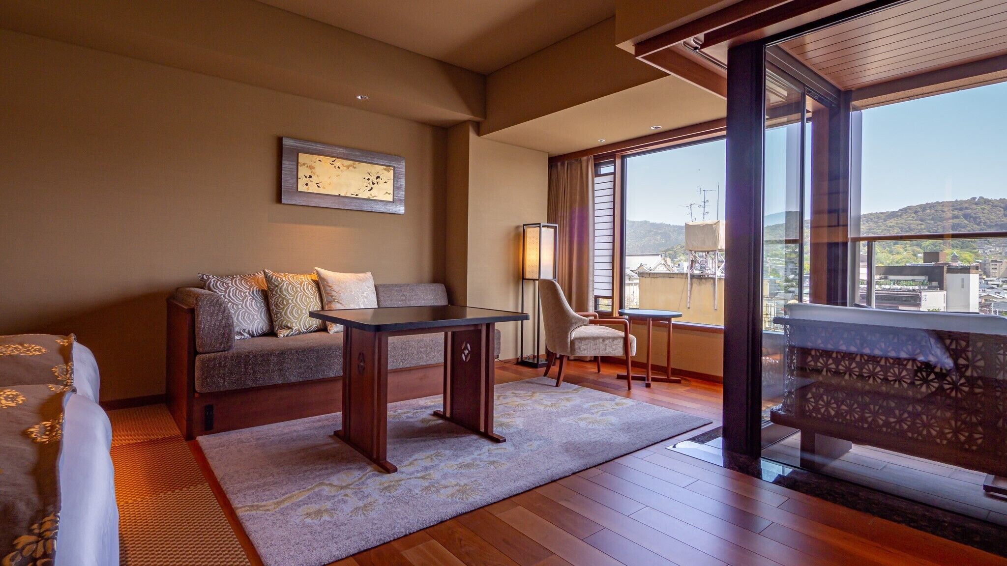 A room with a sofa, a small table, a chair, a lamp, and a view through large windows.