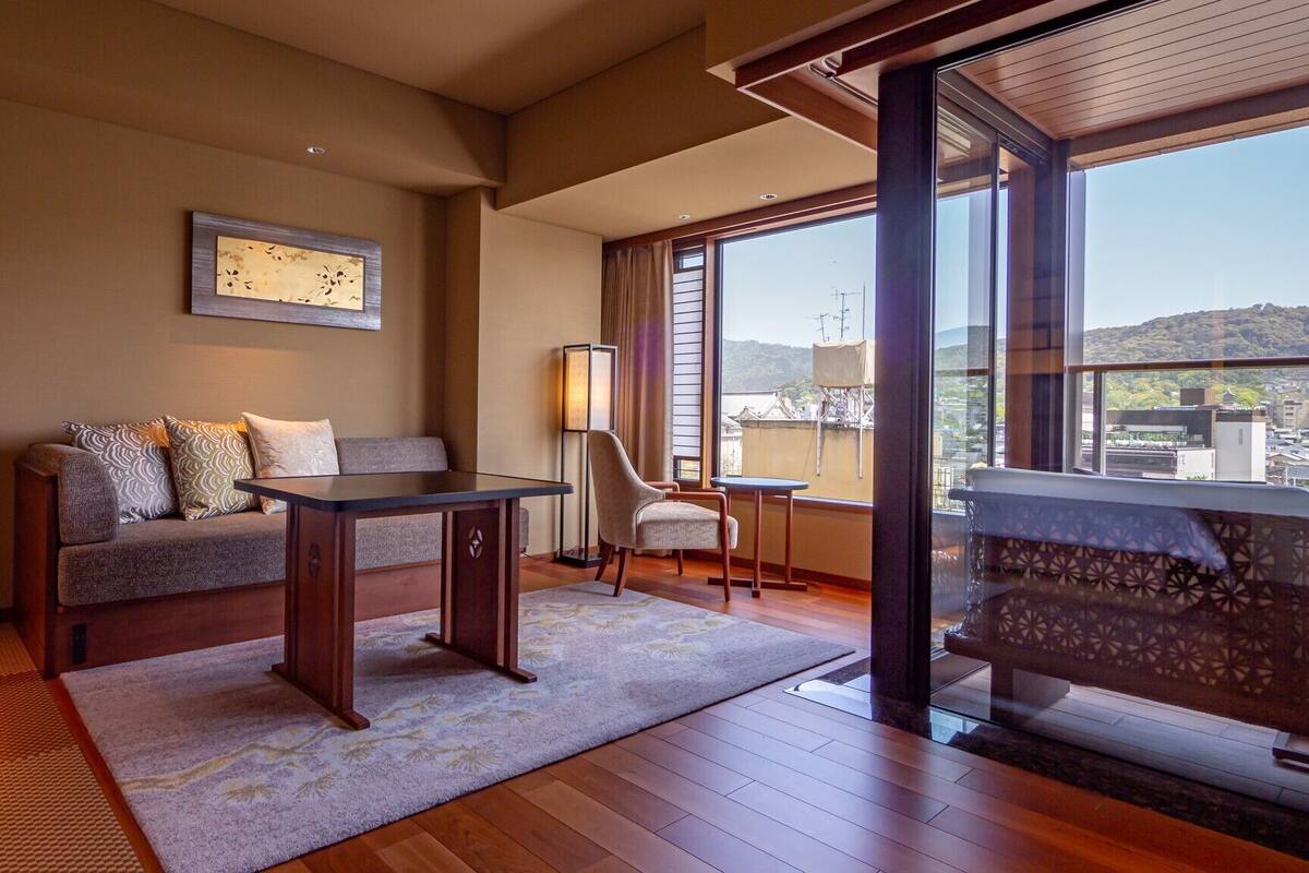 A room with a sofa, a small table, a chair, a lamp, and a view through large windows.