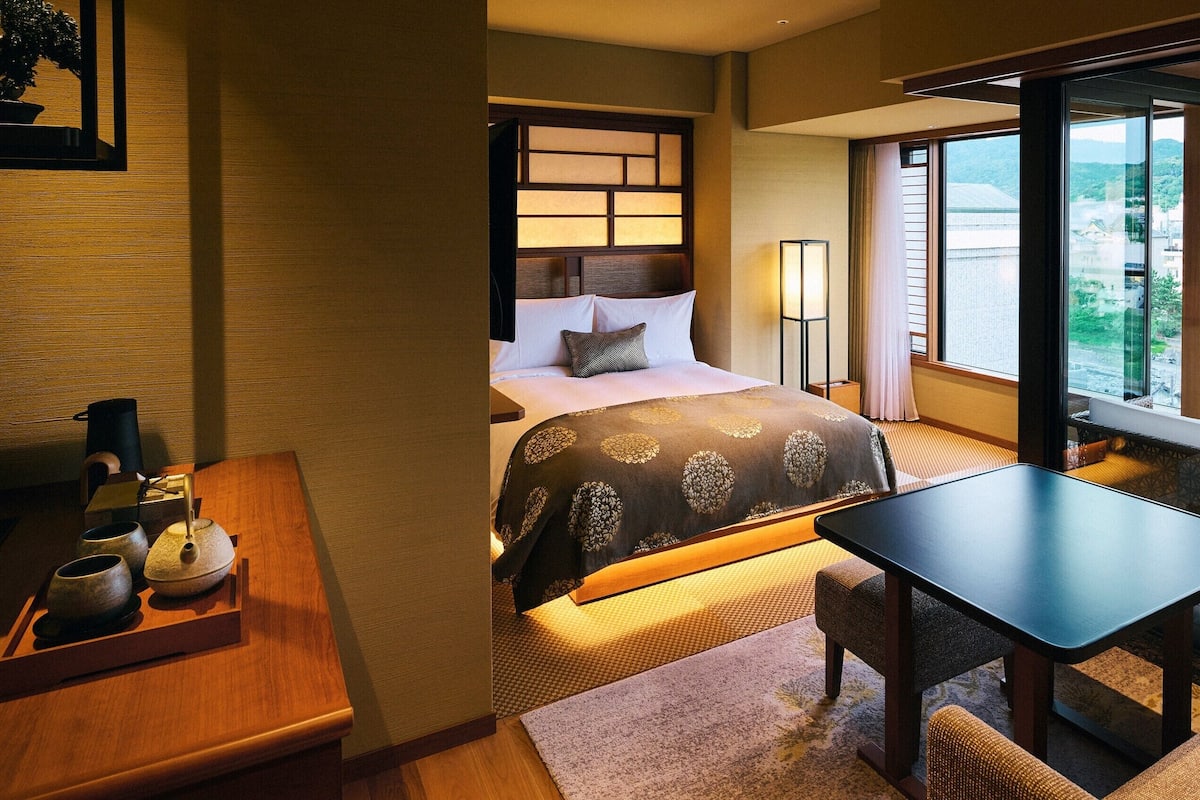 Ein Hotelzimmer mit Bett, Nachttisch, Lampe und Blick auf die Stadt.