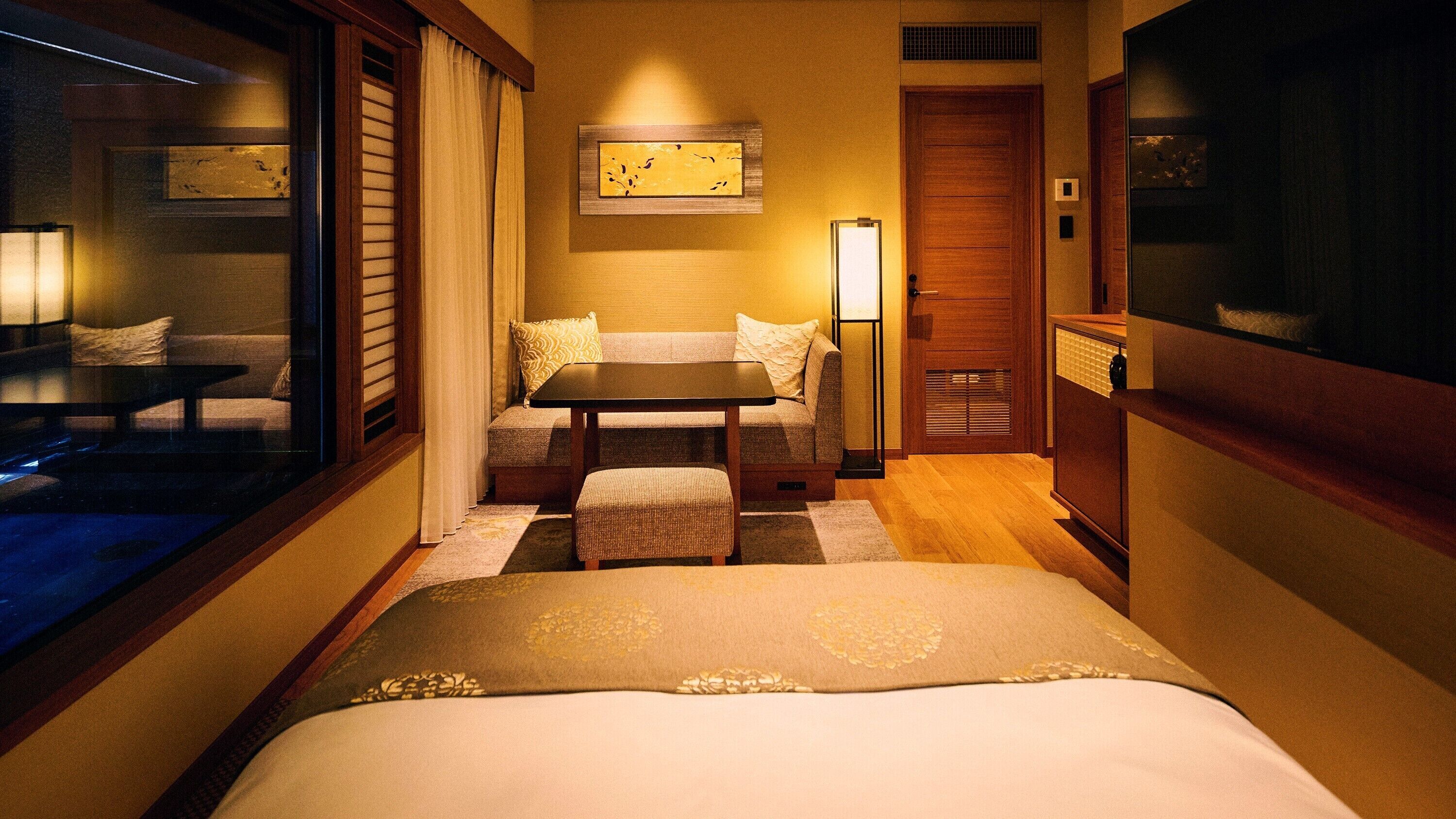 A hotel room with a bed, a small table with two chairs, a lamp, and a painting on the wall.
