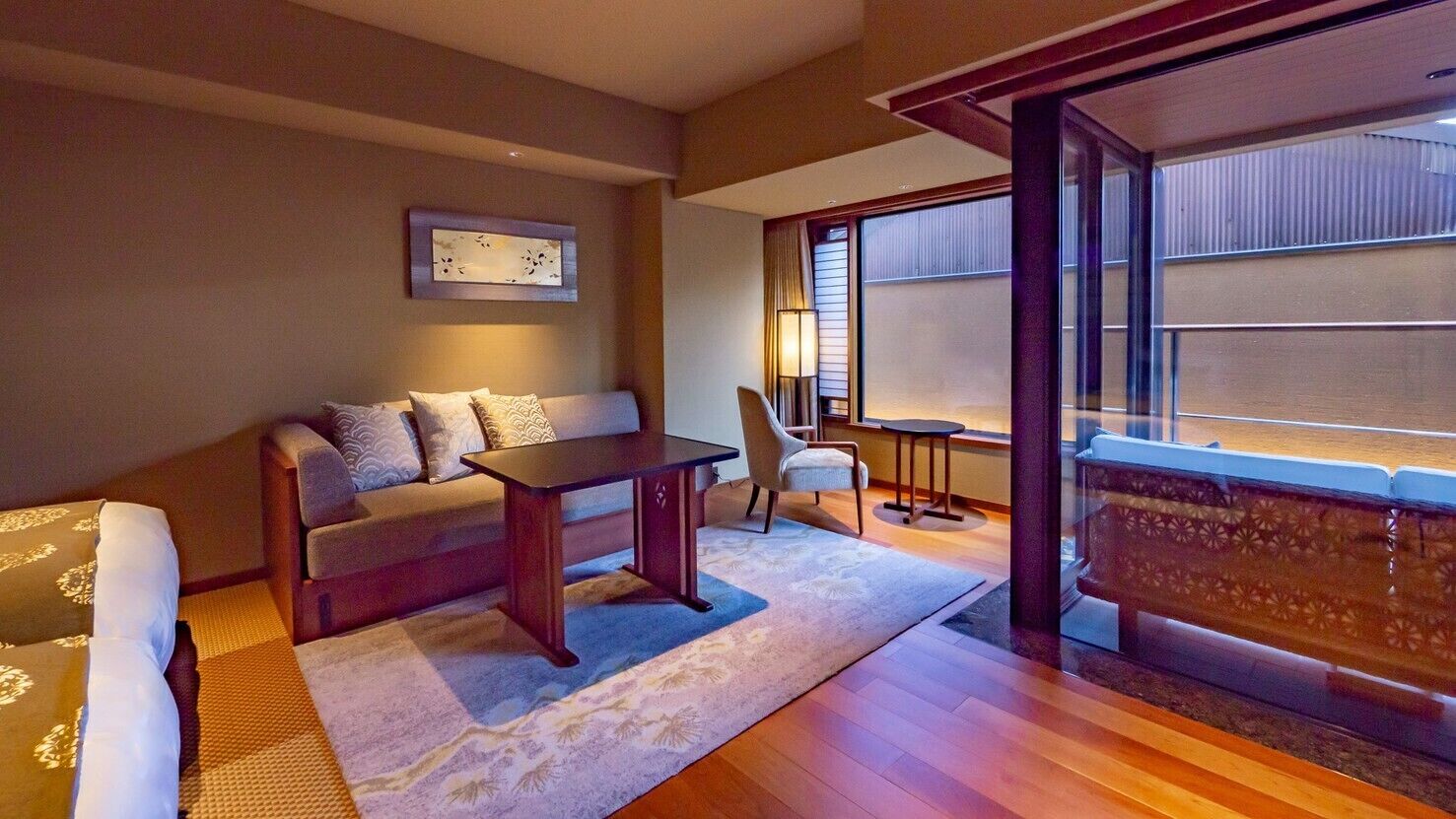 A room with a sofa, a small table, a chair, a lamp, and a view through a window.