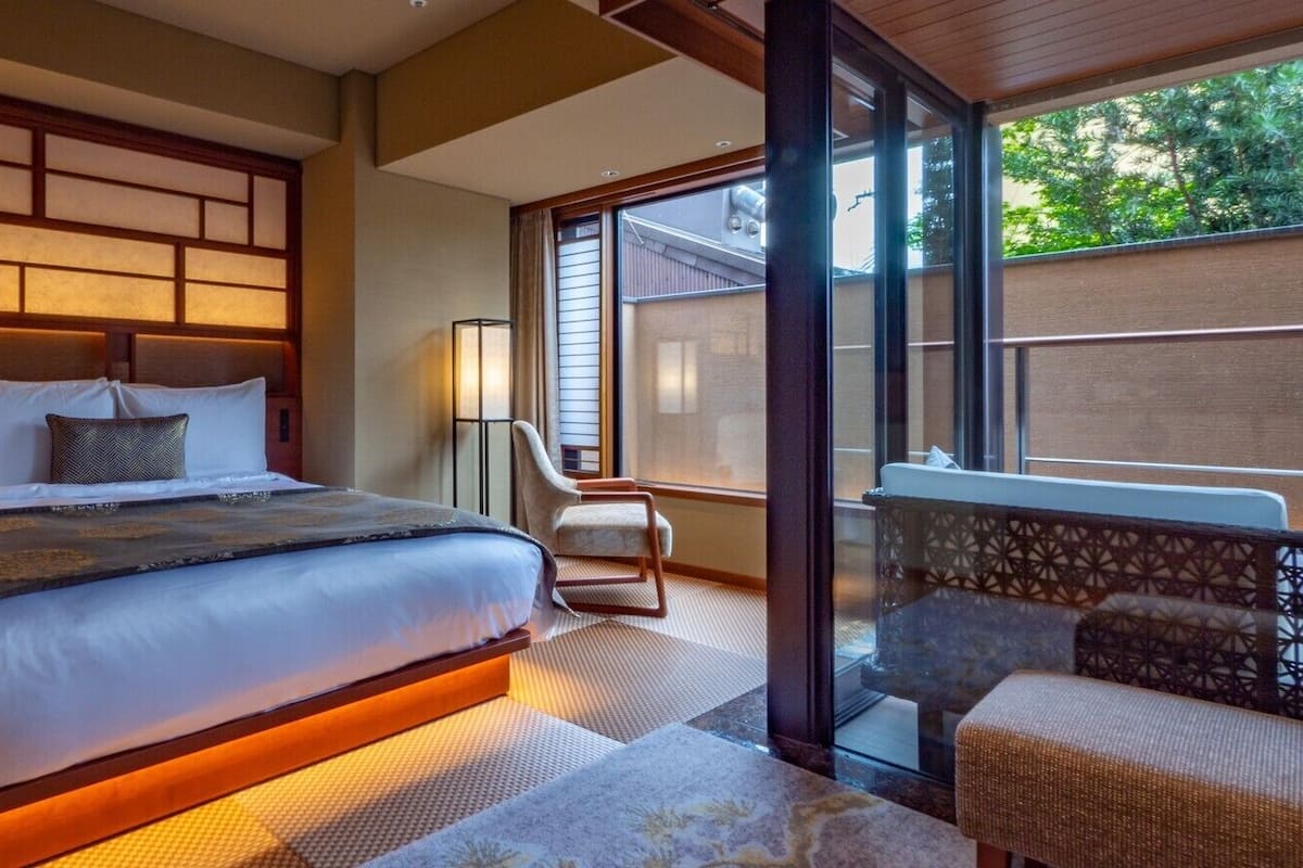 Ein Hotelzimmer mit einem großen Bett, einem Sessel, einem kleinen Tisch und einem Balkon mit Blick.