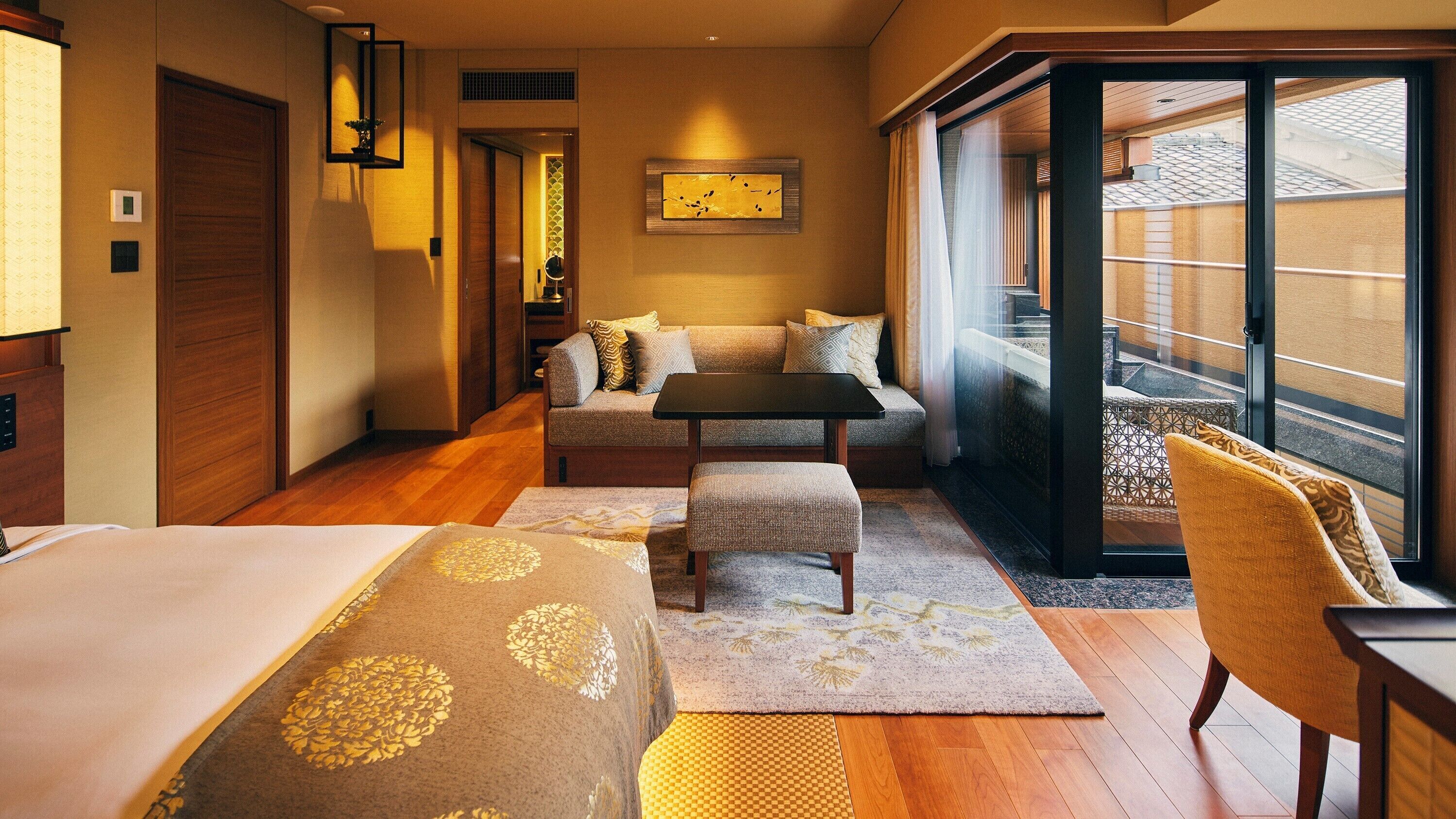 A hotel room with a bed, a sofa, a small table, a chair, and a view of the outside.