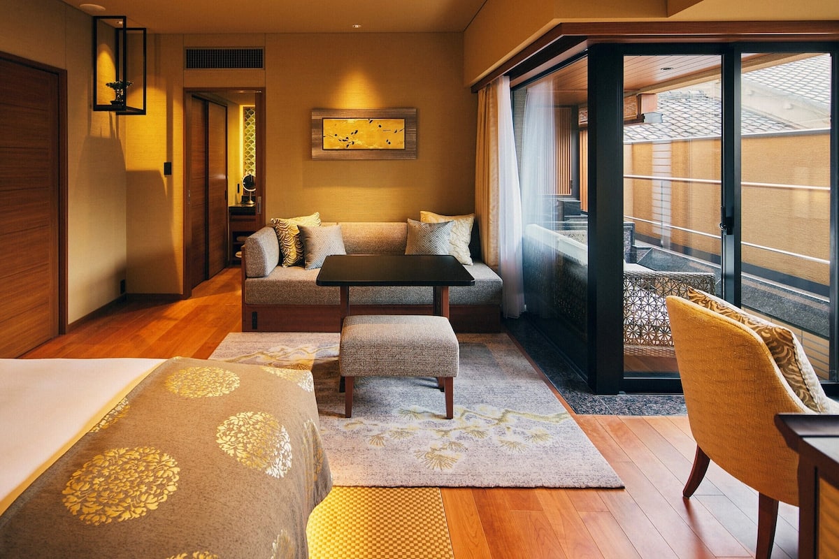 Ein Hotelzimmer mit einem Bett, einem Sofa, einem kleinen Tisch, einem Sessel und Blick ins Freie.