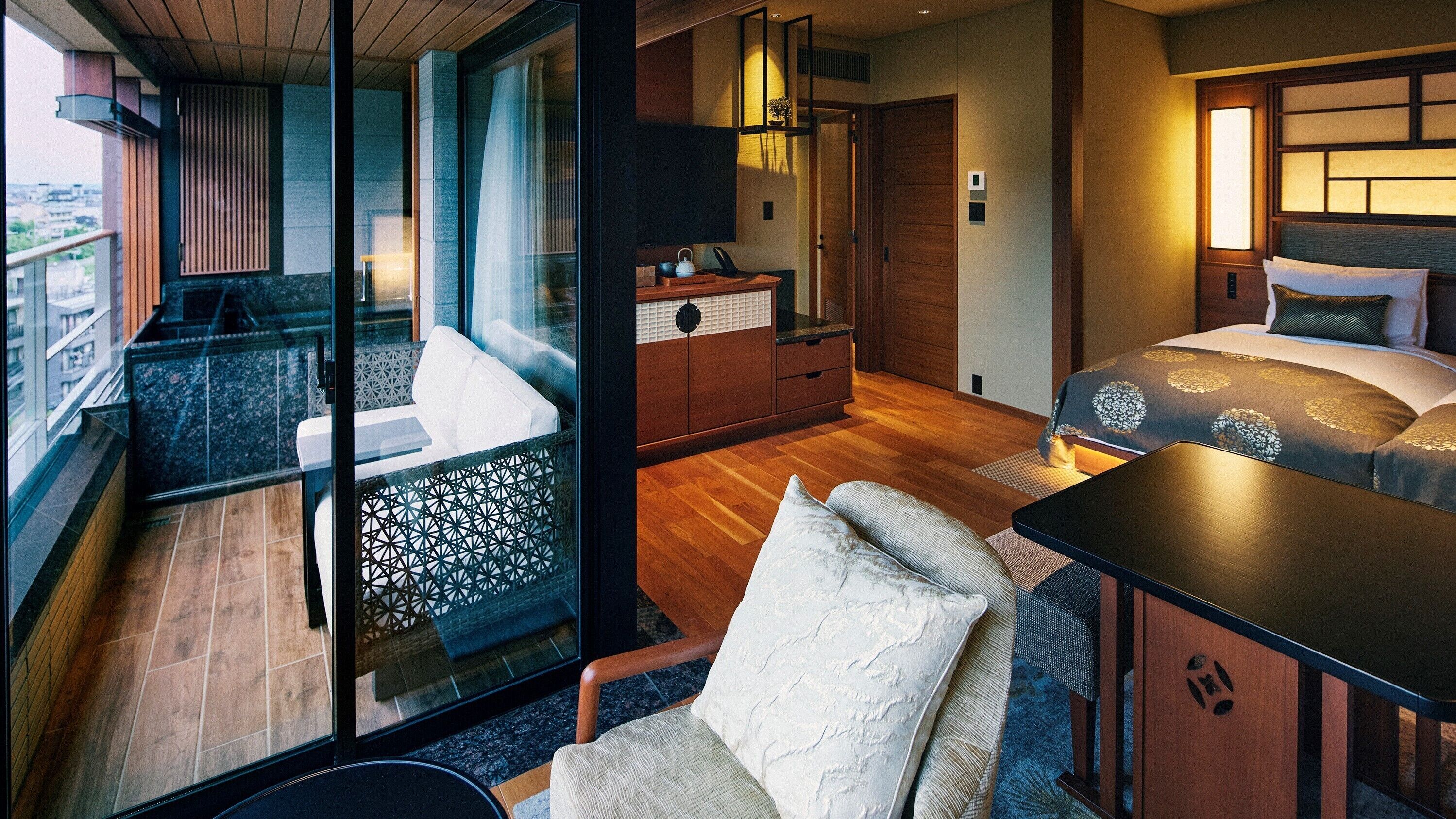A modern hotel room with a balcony, a bed, a desk, and a seating area.