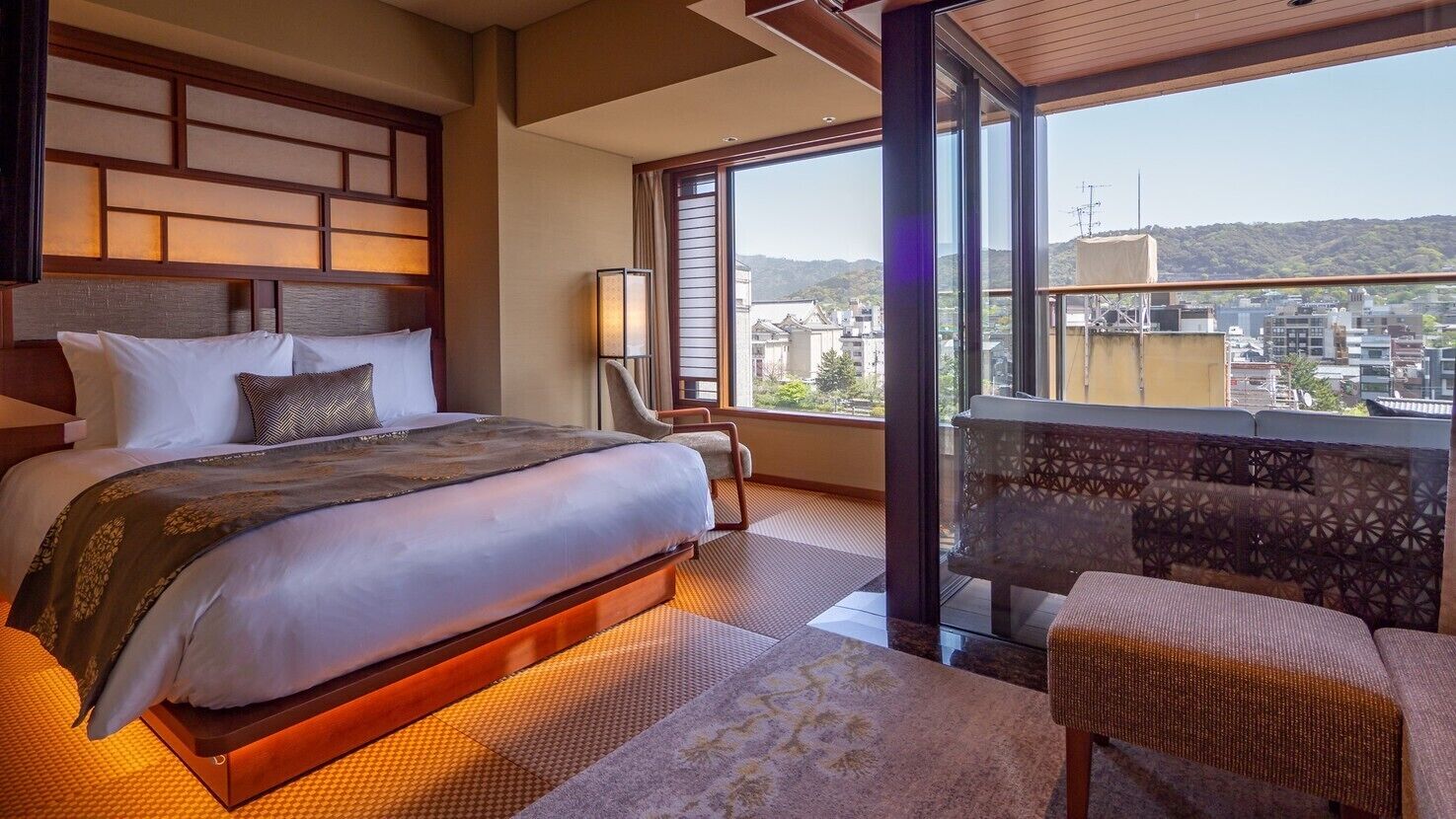 A hotel room with a large bed, a seating area, and a view of the city.