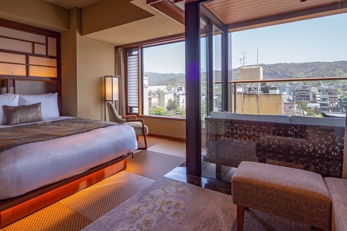 Ein Hotelzimmer mit einem großen Bett, einer Sitzecke und Blick auf die Stadt.