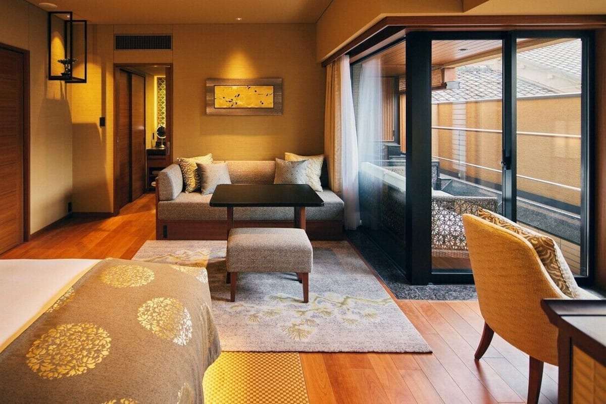 Ein Hotelzimmer mit einer Couch, einem kleinen Tisch, einem Sessel, einem Bett und einer großen Schiebeglasdoor zum Außenbereich.