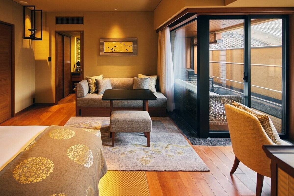 A hotel room with a sofa, a small table, a chair, a bed, and a large sliding glass door to the outside.
