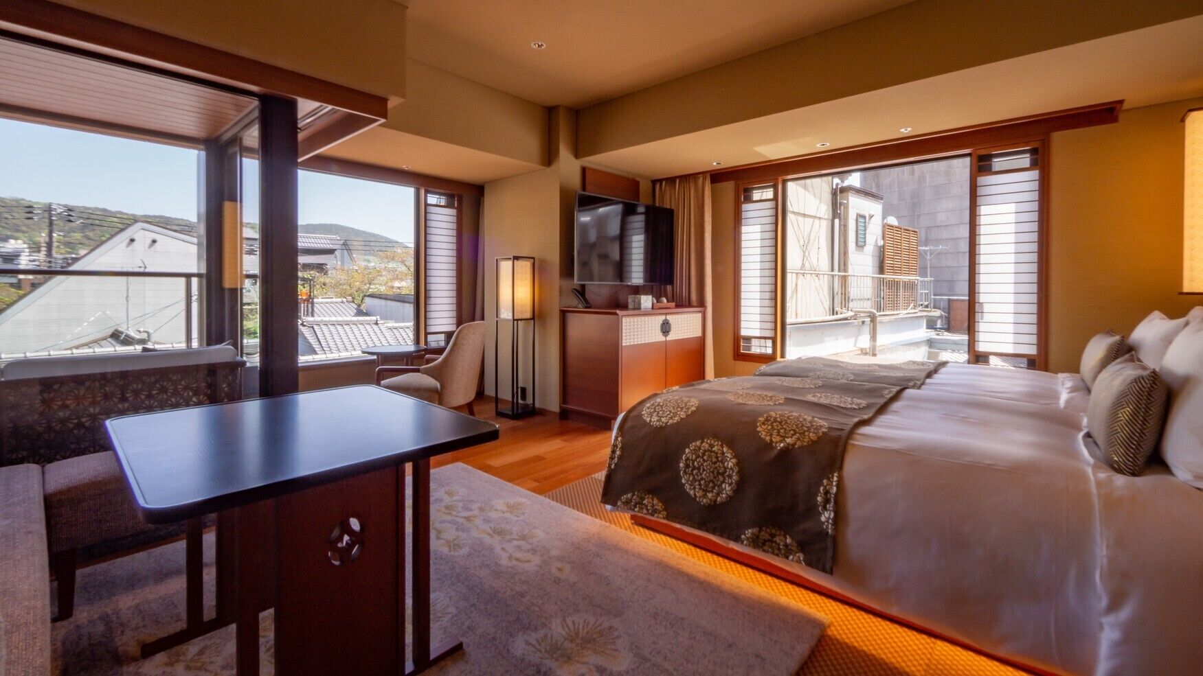 A hotel room with a bed, a desk, a chair, a TV, and large windows.