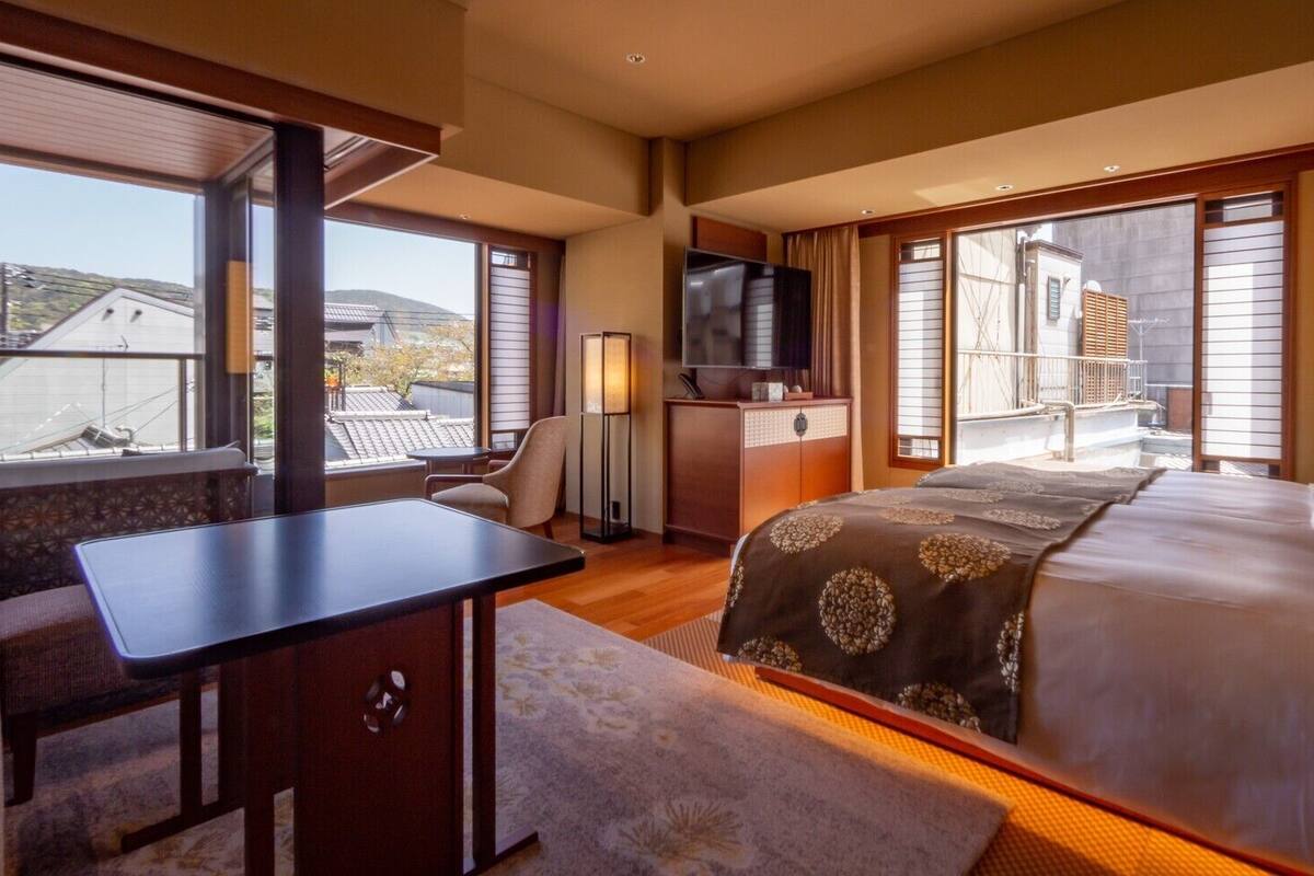 Ein Hotelzimmer mit Bett, Schreibtisch, Stuhl, Fernseher und großen Fenstern.
