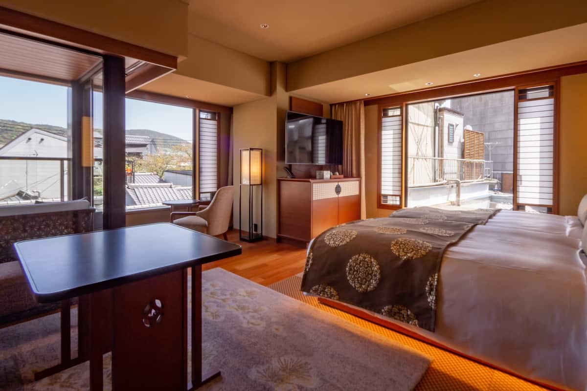 Ein Hotelzimmer mit Bett, Schreibtisch, Stuhl, Fernseher und einem Balkon mit Blick auf Gebäude.