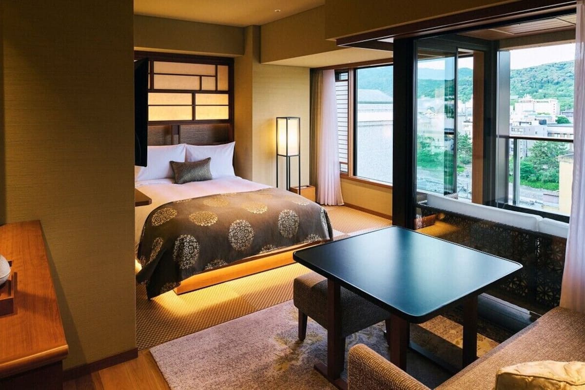 Ein Hotelzimmer mit Bett, Nachttisch, Lampe und Blick auf die Stadt.