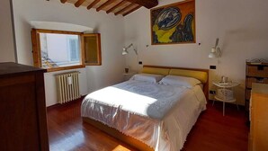 Ein Schlafzimmer mit Holzboden, einem Bett mit weißer Bettdecke, einem Bild an der Wand und einem Fenster mit Jalousien.