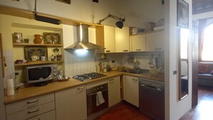 Eine kompakte Küche mit Mikrowelle, Herd, Backofen und Geschirrspüler. Holzschränke, eine Pendelleuchte und ein Fenster sorgen für natürliches Licht.