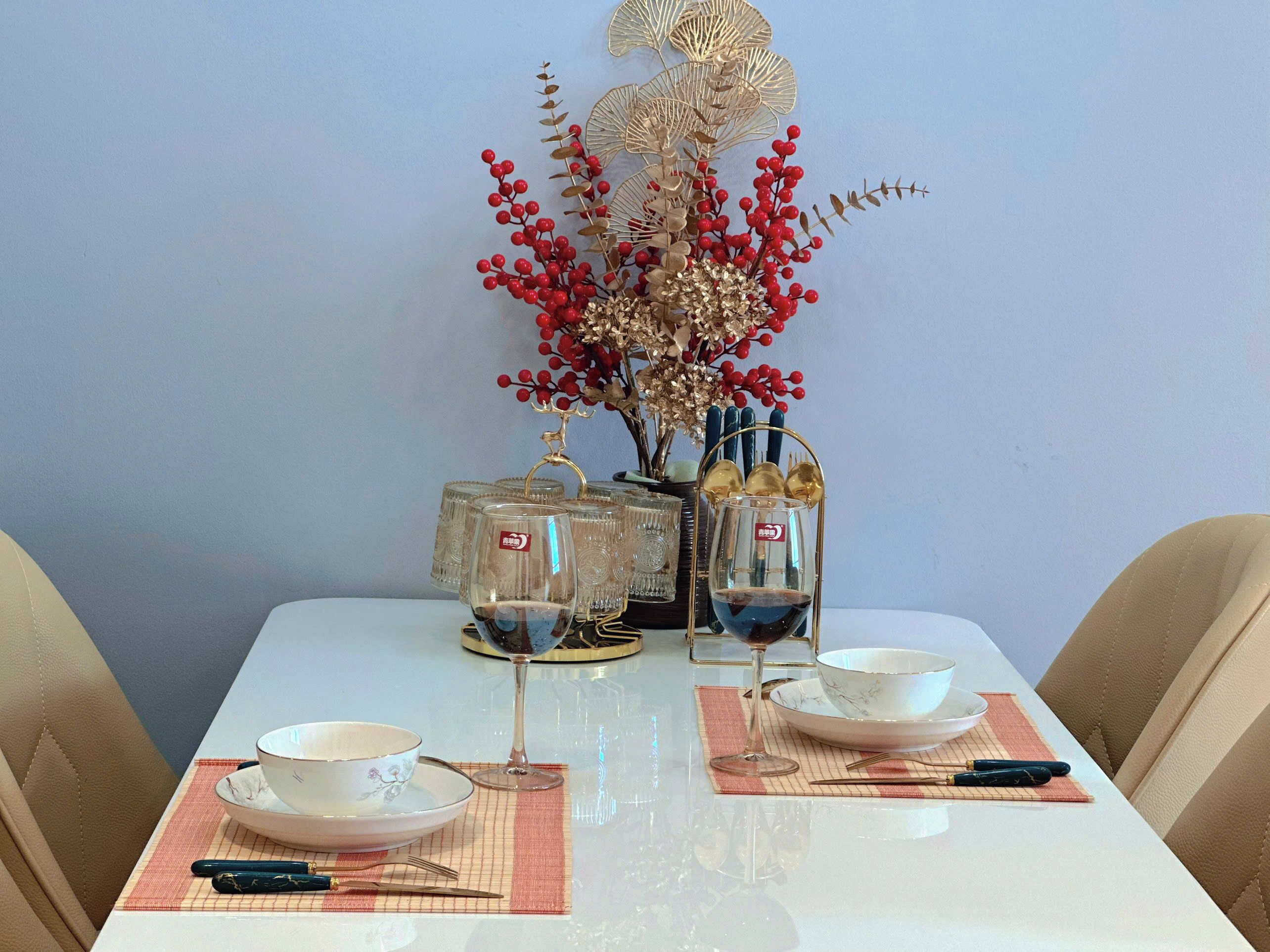 Une table à manger dressée avec de la verrerie, un vase décoratif contenant des baies rouges et un objet de couleur dorée.