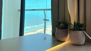 Una habitación con un amplio ventanal con vista al océano, un escritorio de madera y dos plantas en macetas.