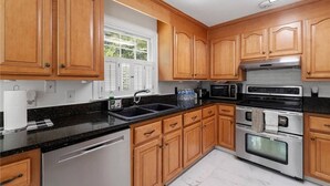 A kitchen with wooden cabinets, a black countertop, stainless steel appliances, and a window with blinds. - Virginia poolside Oasis: your Woodland Escape (Chesterfield)