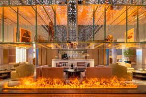 A modern hotel lobby with a glass atrium, a central seating area with sofas, a coffee bar, and a fire feature. - Hilton Garden Inn Ordos Kangbashi (Ordos)