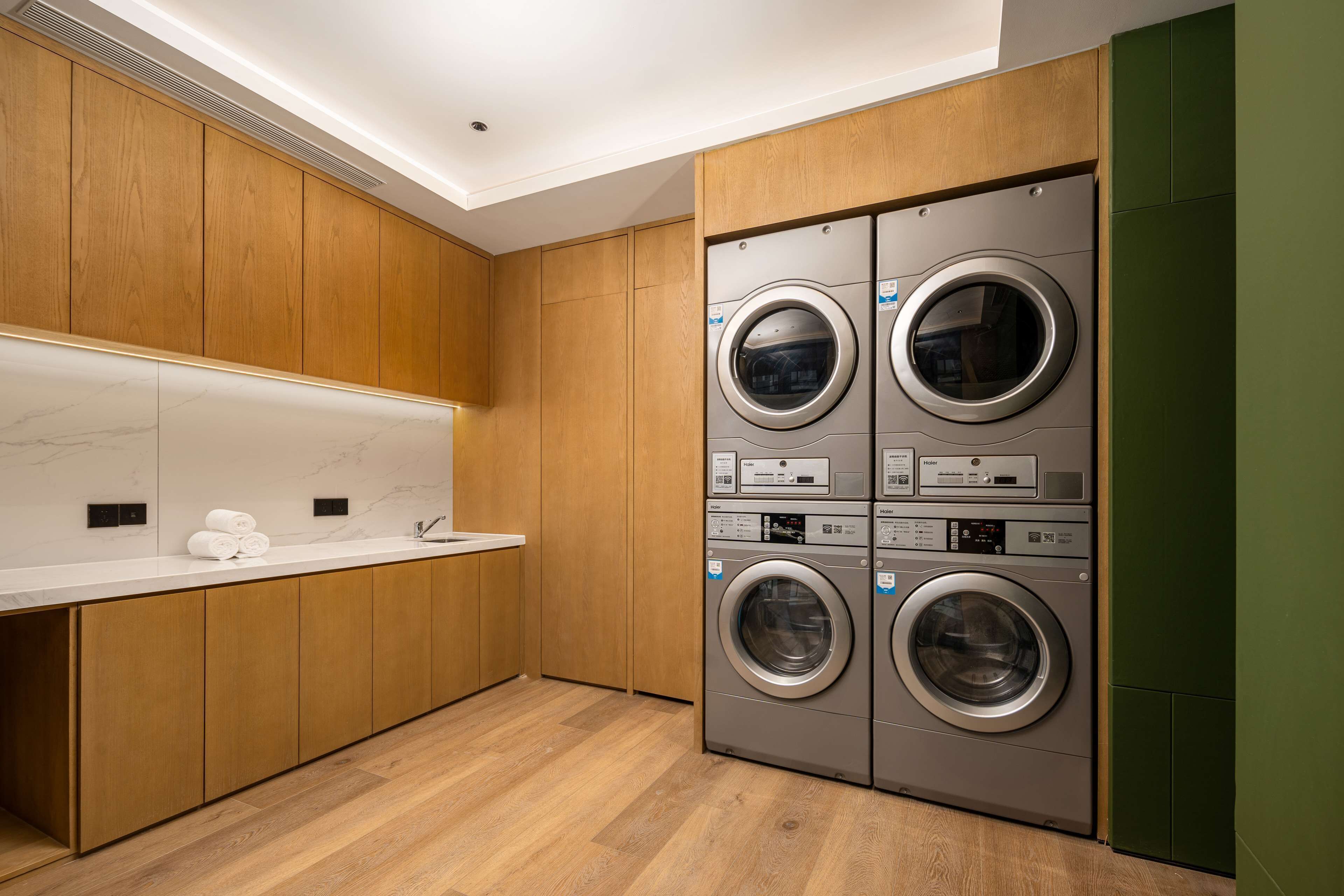 A modern laundry room with wooden cabinets, a marble countertop, and a built-in washer and dryer.