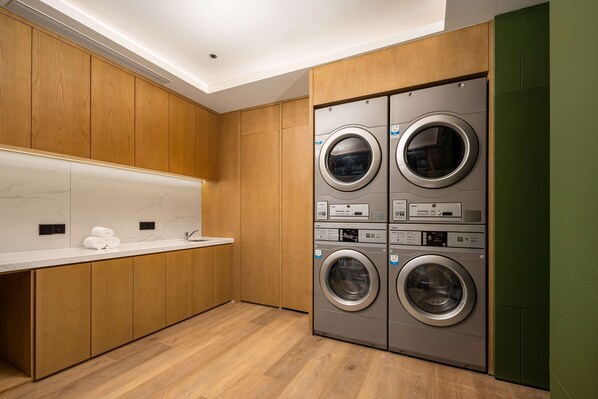 A modern laundry room with wooden cabinets, a marble countertop, and a built-in washer and dryer. - Hilton Garden Inn Ordos Kangbashi (Ordos)