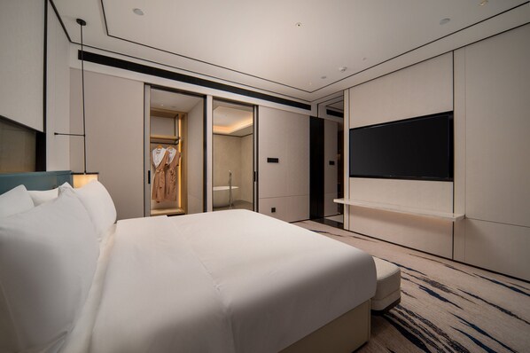 Una habitación de hotel moderna con una cama grande, un televisor montado en la pared y un vestidor.