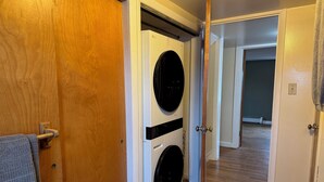 Pesuhuone, jossa on etuaukollinen pesukone ja kuivausrumpu, puiset ovet ja käytävä, joka johtaa toiseen huoneeseen.