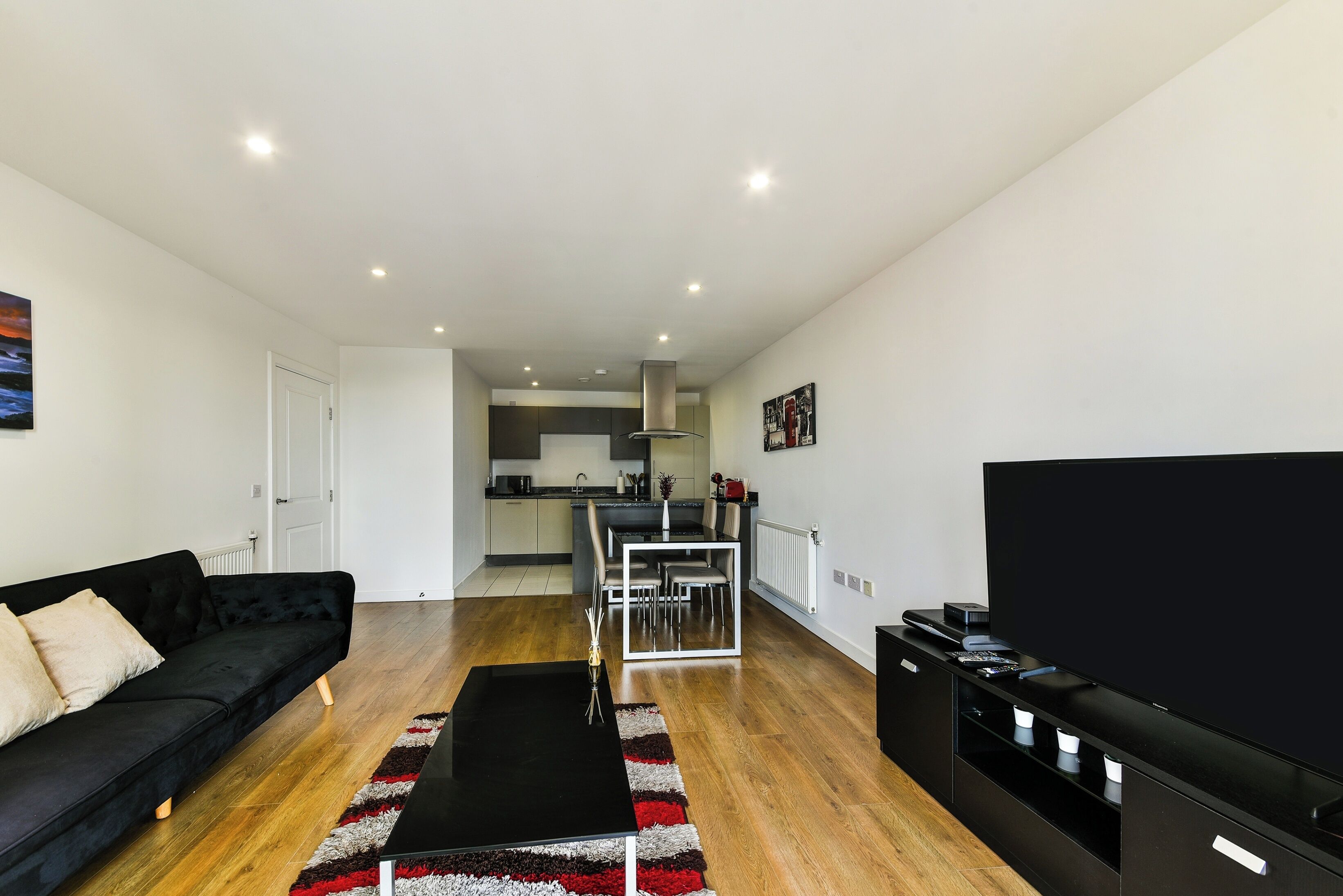 A modern living room with a black sofa, a dining table, and a TV stand.